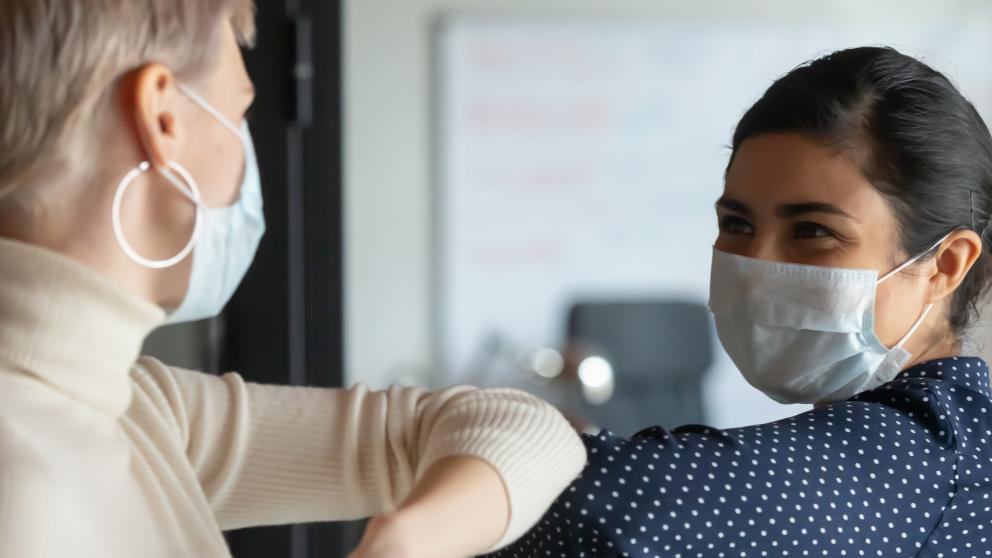 Two happy people greeting by touching elbows, with face masks on.