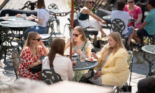 Neljä henkiöä istuu ulkona aurinkoisessa säässä pöydän äärellä, syöden täytekakkua.