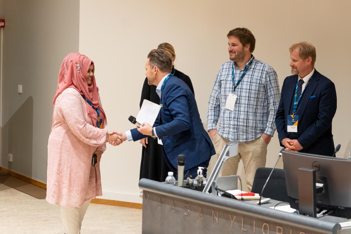 Saraf Fariha Moula and Mikael Hallbäck shake hands, Viktor Sundholm and Kenneth Widell on the background